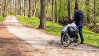 Kaksi henkilöä liikkuu metsässä, toinen on pyörätuolissa.
