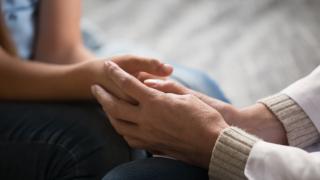 Kaksi henkilöä pitää toisiaan kädestä lempeästi.