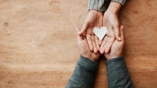 Avoinna olevien kämmenien päällä ovat toiset avoimet kämmenet ja valkoinen paperisydän.