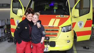 Tittamaria Heinonen ja sairaankuljettaja Meri-Tuuli Lehtonen seisovat vierekkäin ambulanssin edessä.