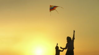 äiti ja lapsi lennättävät leijaa auringonlaskua vasten