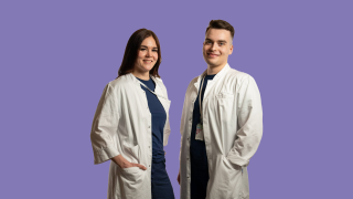 VAKEn lääkärit Saara ja Jani hymyilevät työasuissaan lilaa taustaa vasten.