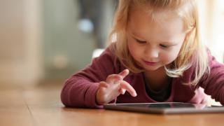 Pieni lapsi makaa lattialla ja käyttää tablet-tietokonetta.