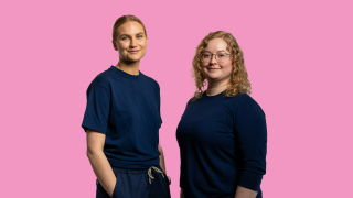 VAKEn sairaanhoitajat Venla ja Ella poseeraavat kuvassa, vaaleanpunaista taustaa vasten.