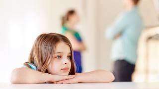 Lähikuva lapsesta, jonka taustalla vanhemmat riitelevät