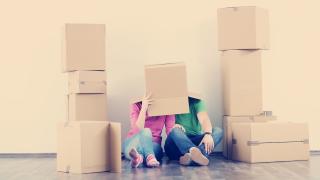 Kaksi henkilöä pahvilaatikossa, ympärillä pahvilaatikoita