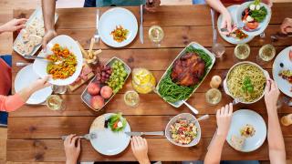 Ihmisiä pöydän ääressä syömässä ylhäältä päin kuvattuna.