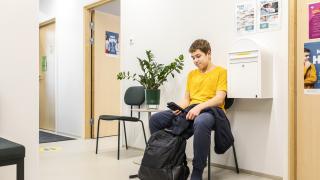 Poika istuu terveydenhoitajan tms vastaanoton käytävässä